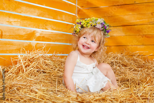 Foto: Beautiful little girl wearing a wreath sitting on the hay Beautiful little girl wearing a wreath sitting on the hay