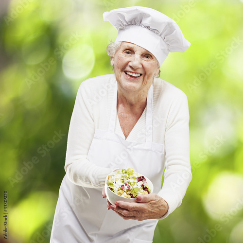 Foto: senior woman cook holding a bowl with salad against a nature bac senior woman cook holding a bowl with salad against a nature bac