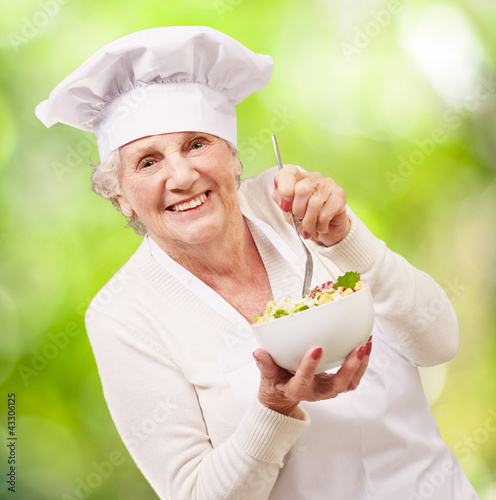 Foto: portrait of adorable senior cook woman eating salad against a na portrait of adorable senior cook woman eating salad against a na