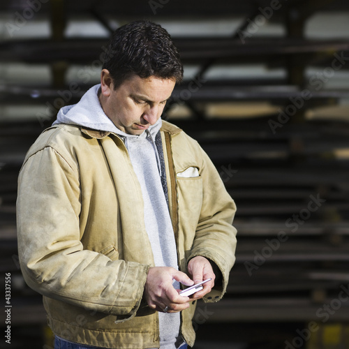 Photo: Caucasian worker using cell phone in factory Caucasian worker using cell phone in factory