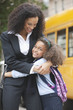 Mixed race mother hugging daughter near school bus