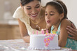 Mother watching daughter blow out birthday candles