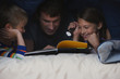 Caucasian father and children reading book under covers