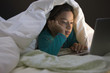 Hispanic girl using laptop underneath covers