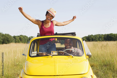 Photo: Woman standing in car sun roof in field Woman standing in car sun roof in field