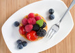 Foto: fruit cake with berries on white plate with a fork, top view fruit cake with berries on white plate with a fork, top view