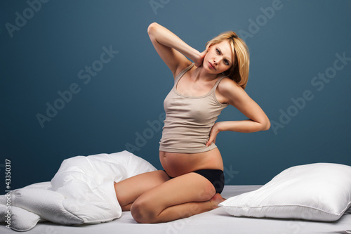 Photo: Tired pregnant woman sitting on bed Tired pregnant woman sitting on bed