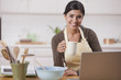 Hispanic woman drinking coffee and looking at laptop
