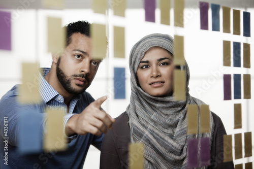 Photo: Business people looking at sticky notes in office Business people looking at sticky notes in office