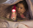 Mixed race girl reading book in bed with flashlight