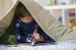 Caucasian boy reading with flashlight underneath blanket