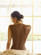 Photo: Woman sitting on massage table looking out with mud mask on her back at luxury spa Woman sitting on massage table looking out with mud mask on her back at luxury spa