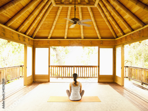 Photo: Rear view of woman sitting in lotus position on floor of yoga and meditation pagoda at a luxury resort Rear view of woman sitting in lotus position on floor of yoga and meditation pagoda at a luxury resort