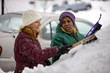 Two women scraping snow from windshield