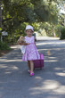 Caucasian girl in dress walking down street with rolling luggage