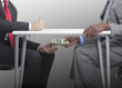 Businessman handing stack of cash under table to co-worker