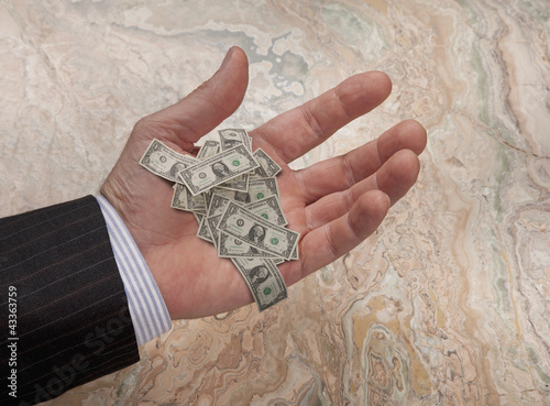 Photo: Caucasian businessman's hand holding tiny dollar bills Caucasian businessman's hand holding tiny dollar bills
