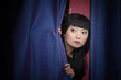 Anxious Asian woman peering out from behind stage curtains