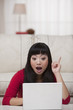Surprised Asian woman sitting on floor in livingroom with laptop