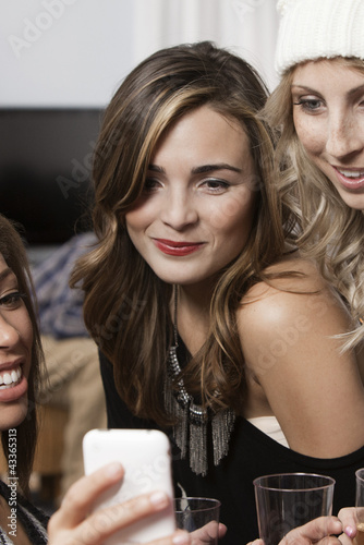 Photo: Friends looking at cell phone at party Friends looking at cell phone at party
