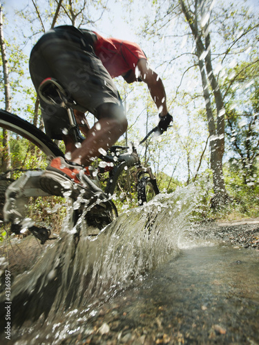 Photo: Mixed race man riding mountain bike through stream Mixed race man riding mountain bike through stream