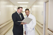Doctor and businessman looking at laptop in hospital corridor