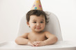 Mixed race girl sitting in high chair wearing party hat