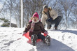 Father watching daughter sledding down snow covered hill