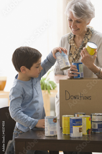 Photo: Caucasian grandmother and grandson filling box with canned goods for charity Caucasian grandmother and grandson filling box with canned goods for charity