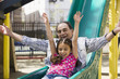 Hispanic grandfather and granddaughter sliding down playground slide