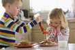 Caucasian boy pouring syrup on sister's pancakes