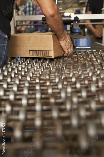 Photo: Worker picking up box from conveyor belt Worker picking up box from conveyor belt