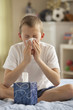Caucasian boy sitting on bed blowing nose