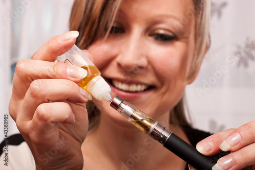 Photo: junge blonde Frau befüllt mit Liquid ihre elektrische Zigarette junge blonde Frau befüllt mit Liquid ihre elektrische Zigarette