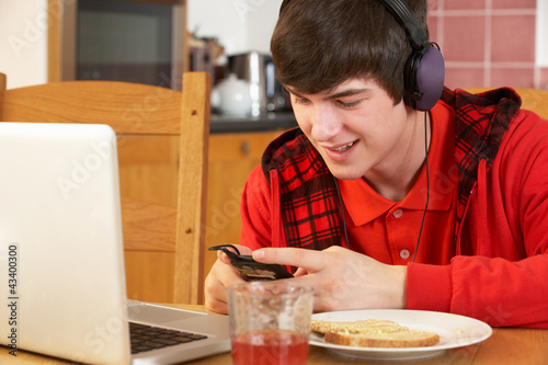 Photo: Teenage Boy Using Laptop And Listening To MP3 Player Whilst Eati Teenage Boy Using Laptop And Listening To MP3 Player Whilst Eati