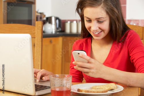 Photo: Teenage Girl Using Laptop And Mobile Phone Whilst Eating Breakfa Teenage Girl Using Laptop And Mobile Phone Whilst Eating Breakfa