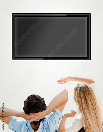Photo: Young couple watching tv. Photo from behind. Lots of copyspace Young couple watching tv. Photo from behind. Lots of copyspace