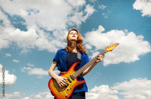 Photo: Redhead girl with guitar at sky background. Redhead girl with guitar at sky background.