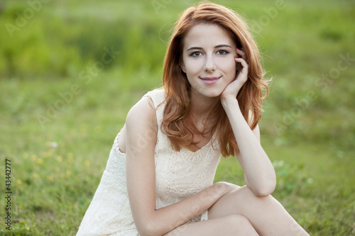 Photo: Redhead girl at green grass at village outdoor. Redhead girl at green grass at village outdoor.
