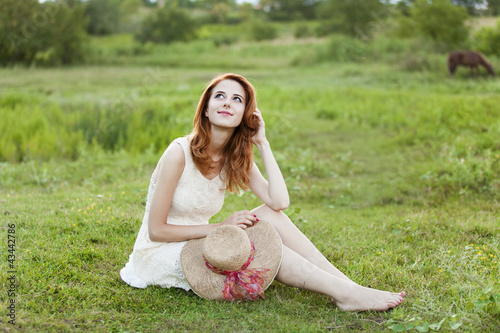 Photo: Redhead girl at green grass at village outdoor. Redhead girl at green grass at village outdoor.