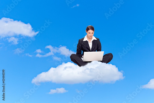 Photo: Young business woman with laptop, sitting on a cloud Young business woman with laptop, sitting on a cloud