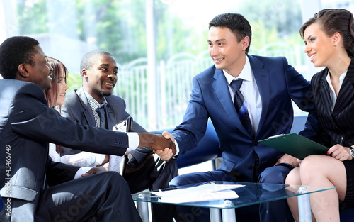 Photo: Two business man shaking hands with his team in office Two business man shaking hands with his team in office