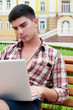 Young man working on laptop while sitting on a bench.