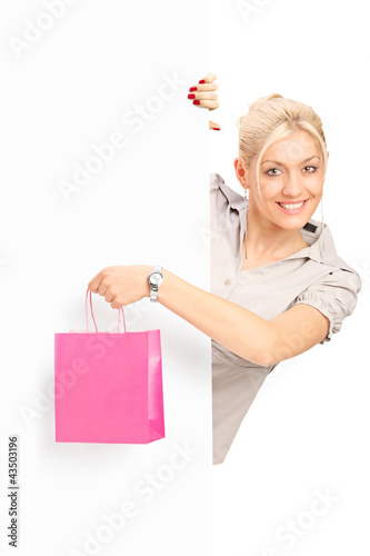 Foto: Smiling young female behind white panel holding a bag Smiling young female behind white panel holding a bag