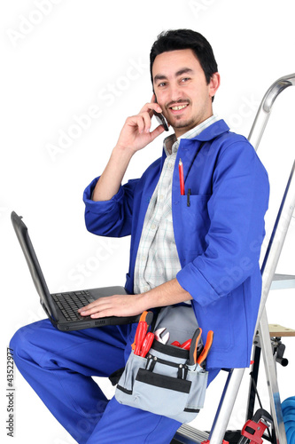 Foto: Plumber sat on step ladder holding mobile telephone Plumber sat on step ladder holding mobile telephone