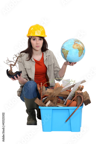 Foto: Woman with globe in hand kneeling by waste materials Woman with globe in hand kneeling by waste materials