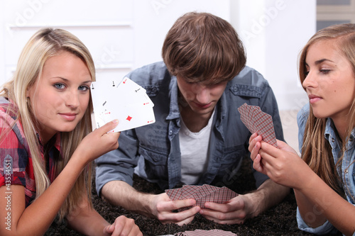 Foto: Three teenagers playing cards. Three teenagers playing cards.