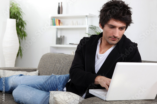 Photo: A young man with his laptop on the sofa. A young man with his laptop on the sofa.