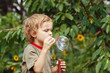 Young blond boy playing with bubbles outdoors on a sunny day