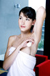Woman in towel applying antiperspirant on her underarm 